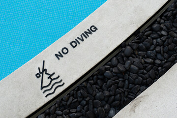 No Diving text warning sign and rules icon at a pool edge with a pictogram beside a blue tiled...