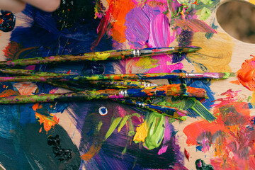 close up pf paint brushes with colourful  paint palette behind 