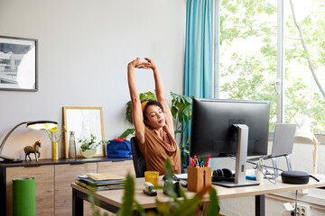 Tired freelancer with raised arms at desk in office