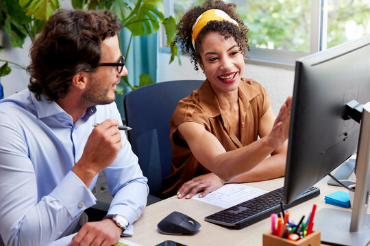 Happy coworkers discussing project on computer at desk