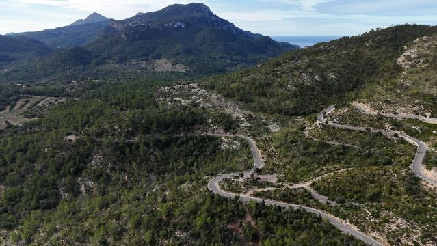 Winding road through green hills under a clear sky in Mallorca, aerial view
