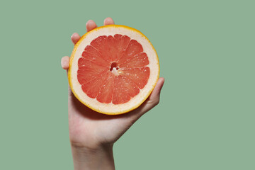 The woman hand squeezes out juice from a ripe grapefruit.