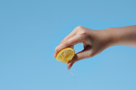 a woman 's hand squeezes a lemon on a blue background