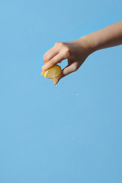 Female hand squeezing half of lemon on blue 