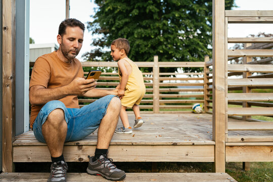 Focused adult father sitting with kid and using smartphone