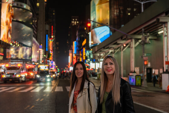Two Happy Tourist Girls Walking In New York At Night.