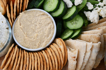 High angle shot of a Charcuterie board with Hummus, pita bread, crackers cucumbers and cheese.