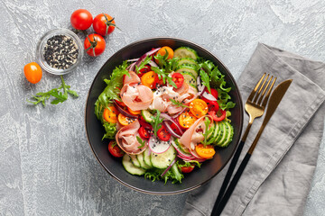 Salad with fresh vegetables and jamon in a black bowl on the table. Top view