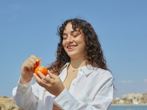 Happy woman with long curly hair eating healthy snack at the beach