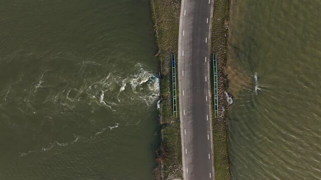 Aerial birdseye view of flood waters passing through a culvert under a road as heavy rains pummel much of Europe