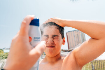 Spraying sunscreen on teen's face. 