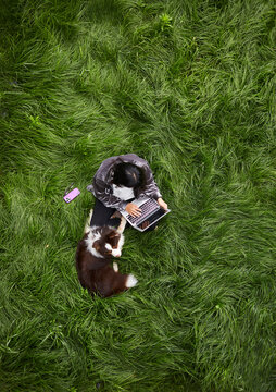 Asian woman using laptop and dog outdoors on beautiful grass