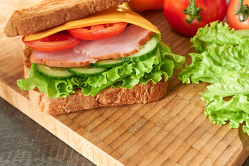 Sandwich with ham, cheese and vegetables on a wooden board.