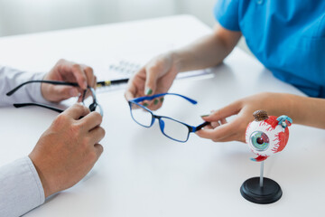 Female doctor talking with patient in clinic room at table Focusing on eye health with male patients. and use eye models and eyeglasses to discuss vision health.