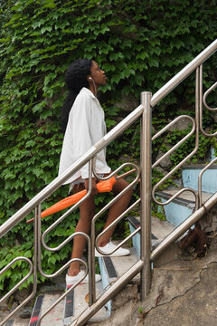 A woman with a orange umbrella going upstairs beside green leaves
