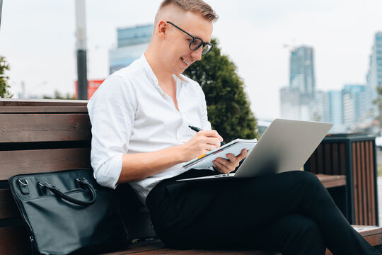 Confident businessman sitting outdoor working online make notes