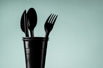Disposable black plastic cup and cutlery on a gray background. Ecology and recycling concept.