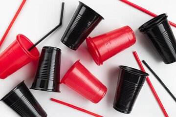 Plastic red and black cups with drinking straws on a white background. Close-up, studio shot.