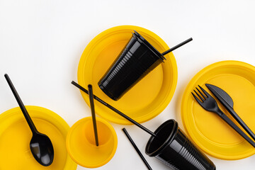 A set of disposable plastic tableware in lilac, yellow and black colors. Ecology and plastic waste recycling concept.