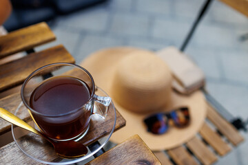 Coffee is on a table in a street coffee shop, and a hat and glasses are on a chair nearby.
