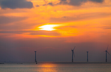 Sunset on the beach with offshore wind power generators visible on the horizon. wind force, Offshore Wind Power