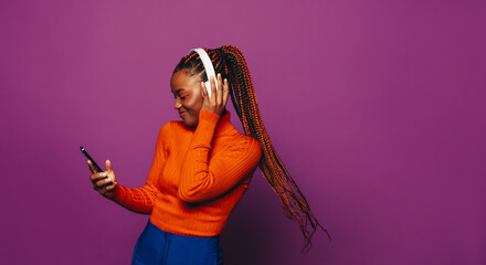 Happy gen z woman dancing with headphones and phone on purple background.