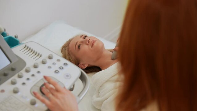 Professional female endocrinologist performing ultrasound examination of lymph nodes of patient neck. Diagnosis and treatment of autoimmune thyroiditis concept. Shooting in slow motion.