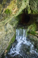 Wild cave outside. The river flows out of the cave, a waterfall. Speleology and surveys
