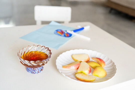 Honey and Plate of Sliced Apples on Table with Children's Drawing.