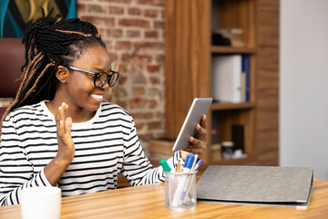 Smiling Afro American woman engaged in a video call while seated at her home office, showcasing...