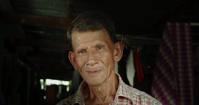 A smiling Asian man who is an elderly worker live in a poor dark house. Used in film concepts, humanity, documentaries and others.