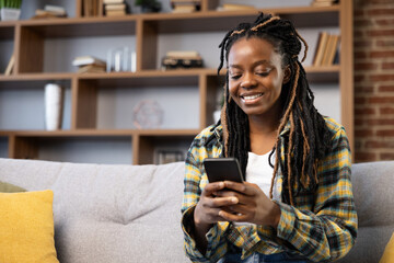 Woman Using Smartphone at Cozy Home . Afro American Female enjoying moment using phone at home....