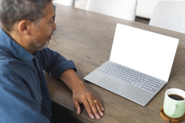 Fototapeta na wymiar Biracial senior man with graying hair works on a laptop at a wooden table, with copy space