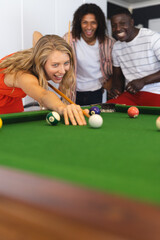 Young Caucasian woman plays pool as biracial and African American men watch, with copy space