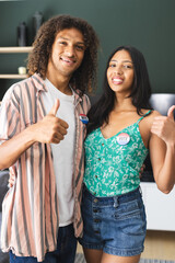 Biracial couple with "I Voted" stickers give thumbs up, smiling confidently
