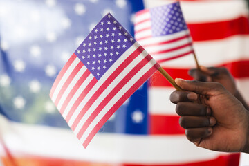 African American hand holding an American flag with another flag in the background