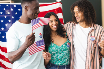 African American man and biracial couple hold American flags, all wearing I Voted stickers