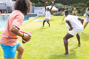 Young African American man prepares to throw a football at a backyard party