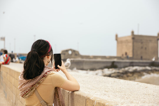 A young woman taking photos with her smartphone in Essaouira, Morocco