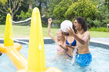 Young Caucasian woman and biracial man play volleyball in a pool