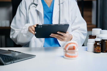 Dentist sitting at table with jaw samples tooth model and working with tablet and laptop in dental modern office