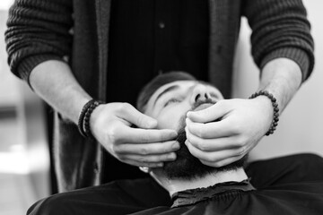 A barber massages and rubs a male client beard after applying moisturizing oil