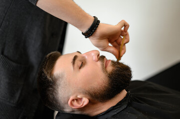 Barber combs beard with comb while shaving Caucasian man