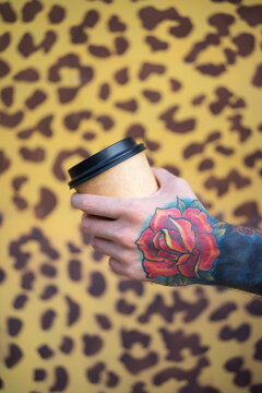 Man with a tattoo holds a coffee cup in his hand