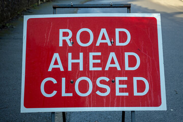 A large red roadworks sign on a road warning that the road ahead is closed