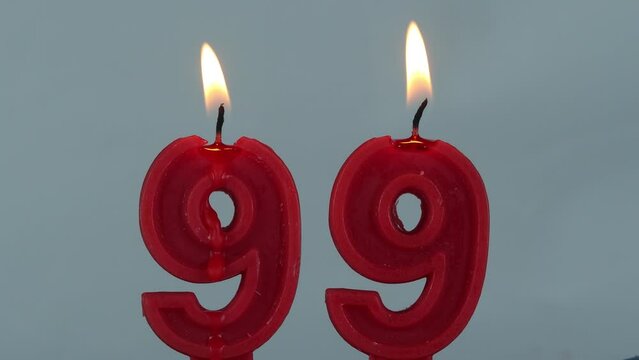 close up on timelapse melting a red number ninety nine birthday candle on a white background.
