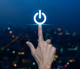 Hand pressing power button icon over blur colorful night light modern city tower and skyscraper,...
