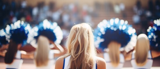 A group of cheerleaders, clad in matching uniforms with blue pompons, stand in front of a mirror, their reflections bouncing back. The basketball court provides a backdrop to their synchronized - obrazy, fototapety, plakaty