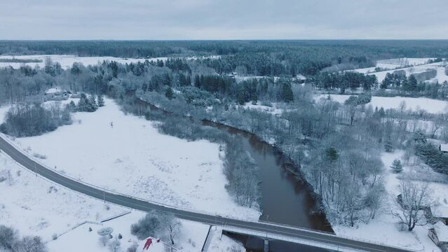 Abava river winding through a snowy landscape near Renda village (Kuldiga parish, Latvia), winter setting, aerial view, moving backward, tilt down
