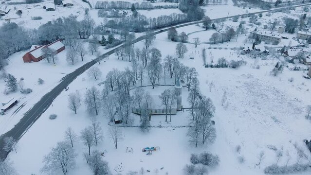 Snow-covered landscape with roads and colorful playground in Renda village (Kuldiga parish, Latvia), winter scenery, aerial view, moving forward, tilt down